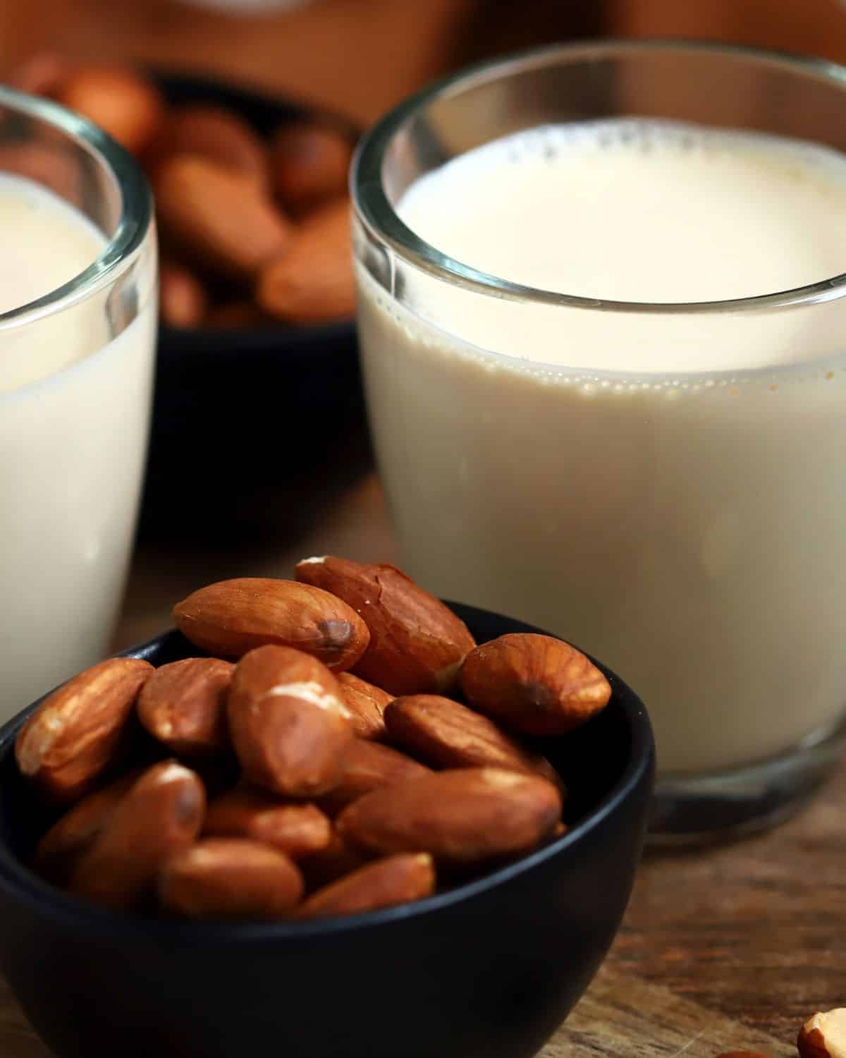 2 cups of almond milk with a bowl of almonds in front 