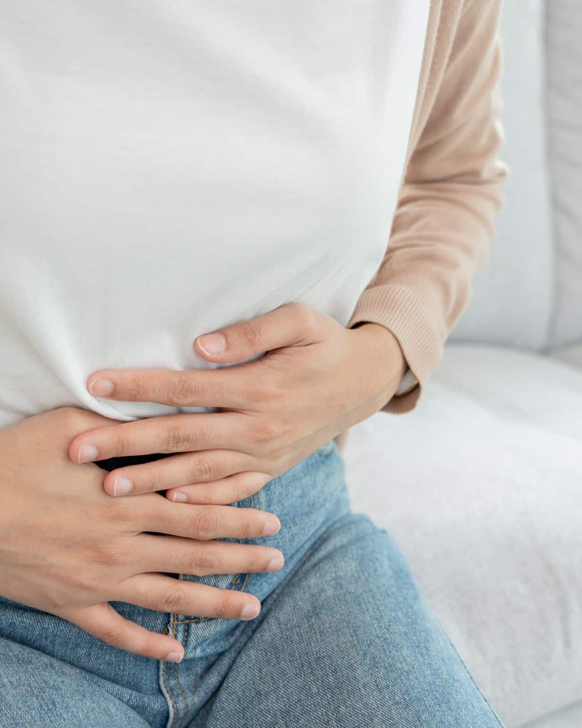 person wearing jeans and white t shirt cramping stomach 