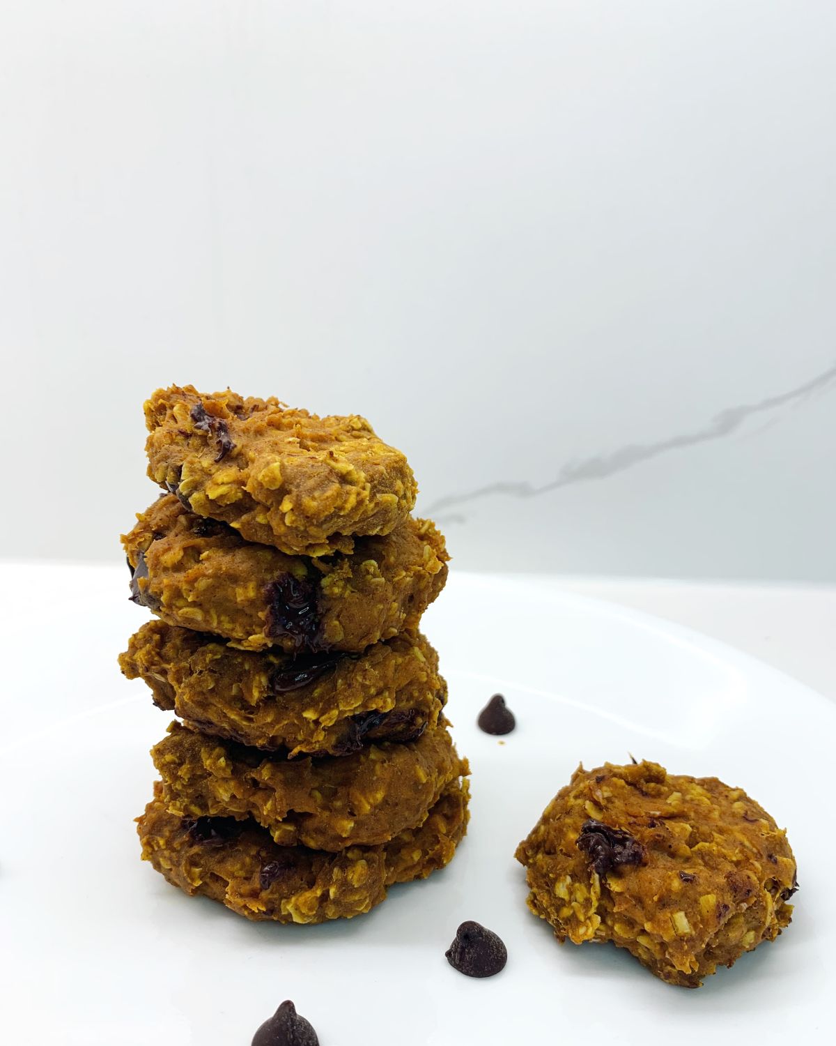 stack of 5 healthy pumpkin pie cookies on a plate - chocolate chips all over the plate scattered and one cookie off to the side 