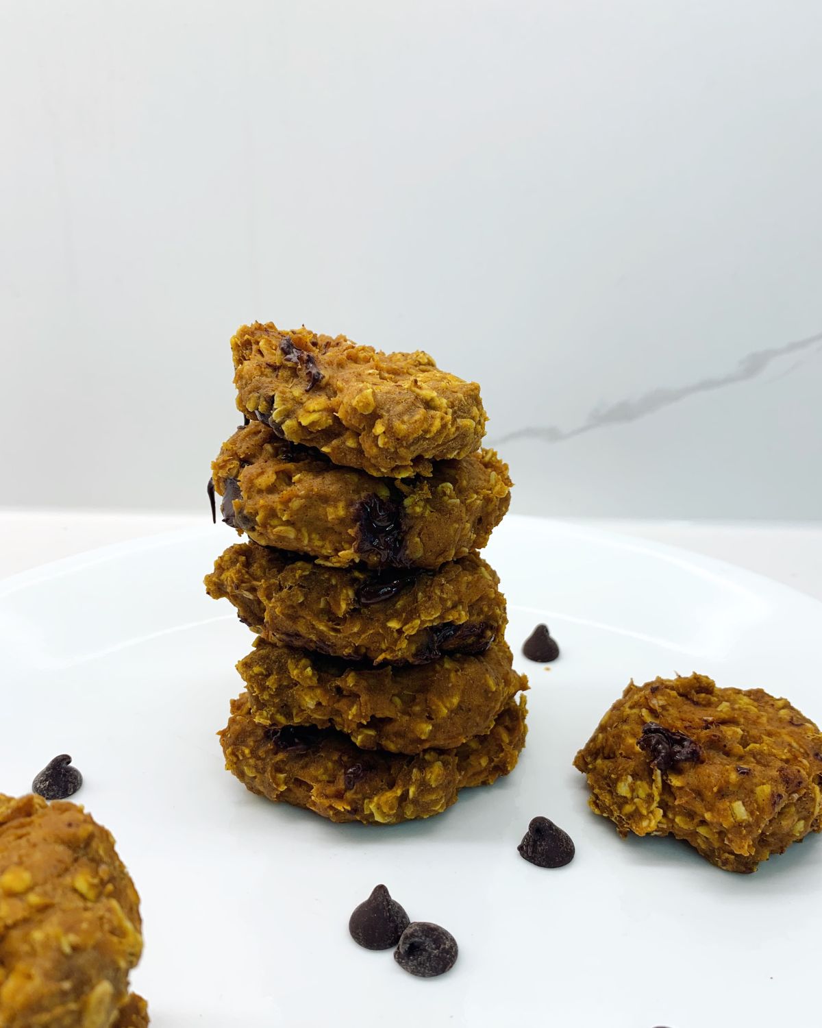 stack of 5 cookies with 2 around the stack with some chocolate chips around plate 