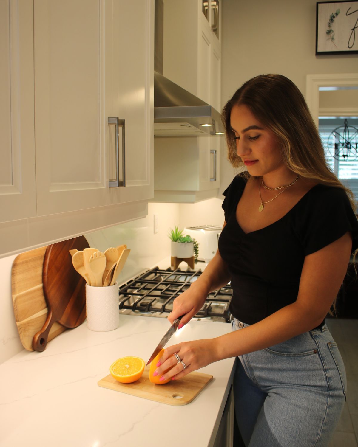 registered dietitian standing in kitchen cutting up an orange - wearing jeans and black t shirt 