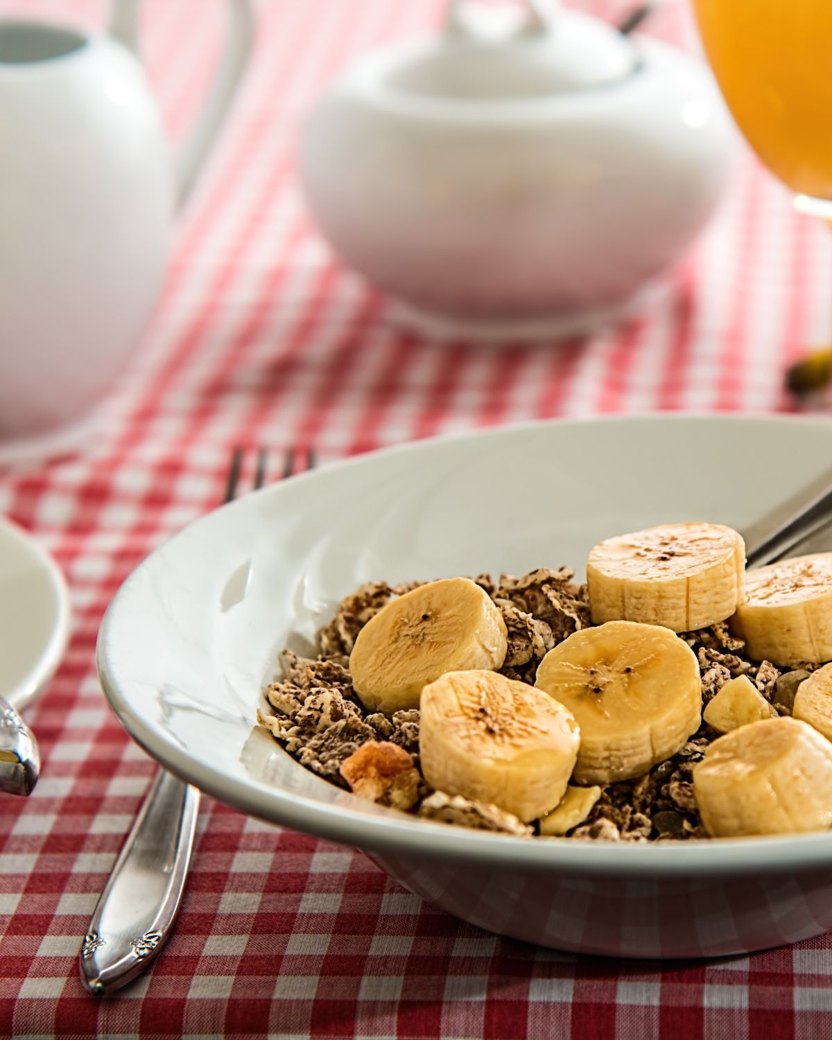 big white bowl on table with a red checker table cloth - inside bowl is a high fibre grain cereal with banana slices. 