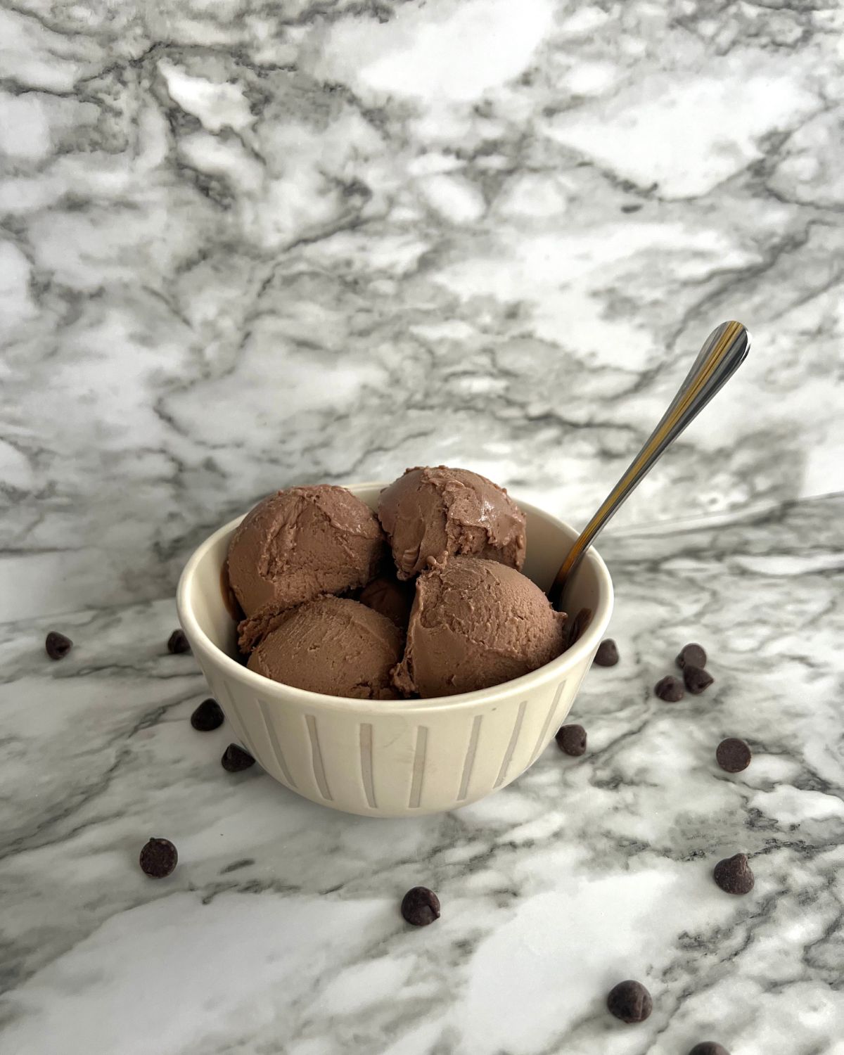 scoop of ice cream in bowl with spoon in it chocolate chips scattered around