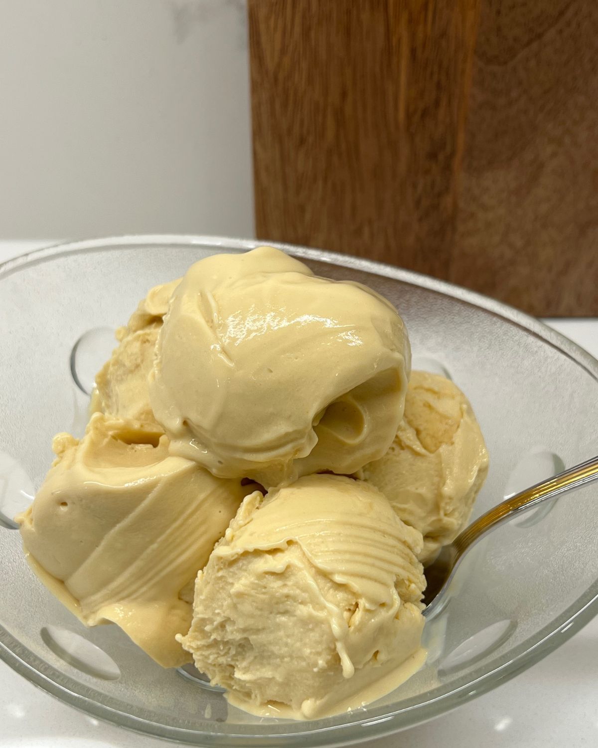 close up of vanilla ice cream in bowl on counter in front of brown cutting board 