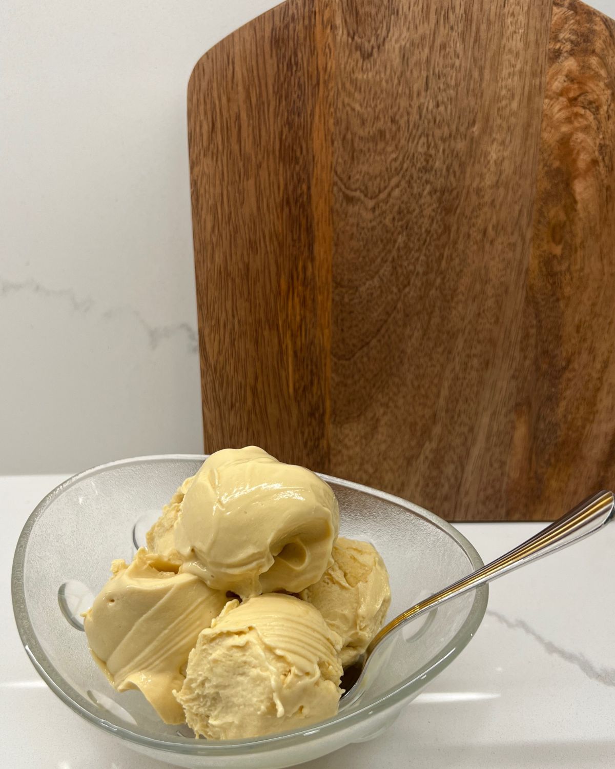 vanilla ice cream in bowl on counter in front of brown cutting board 