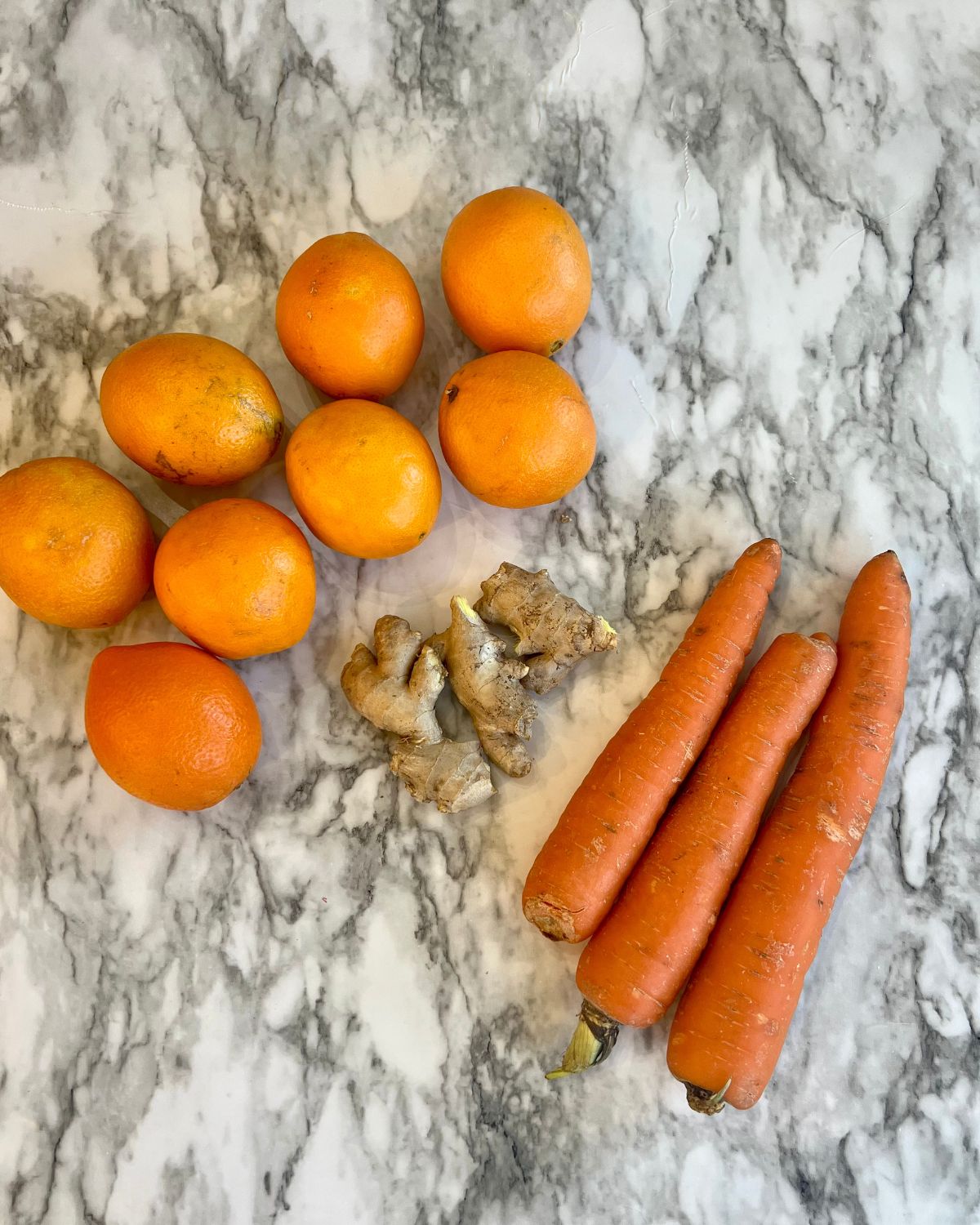 Oranges, carrots and ginger laid out on table before they have been cut 