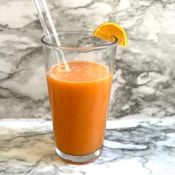 glass of orange carrot ginger juice with glass straw