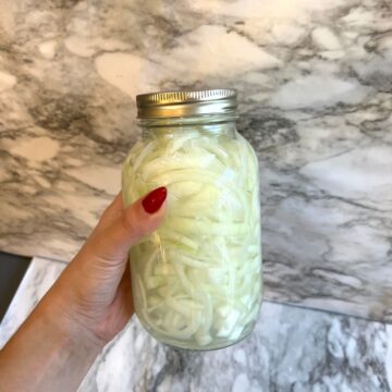 holding up a mason jar filled with pickled white onions