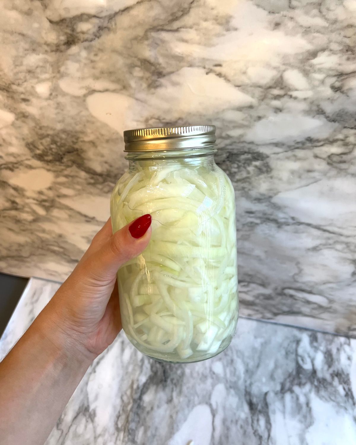 holding up a mason jar filled with pickled white onions