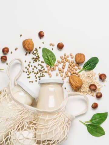 two containers of plant based milk with nuts and seeds scattered around the table