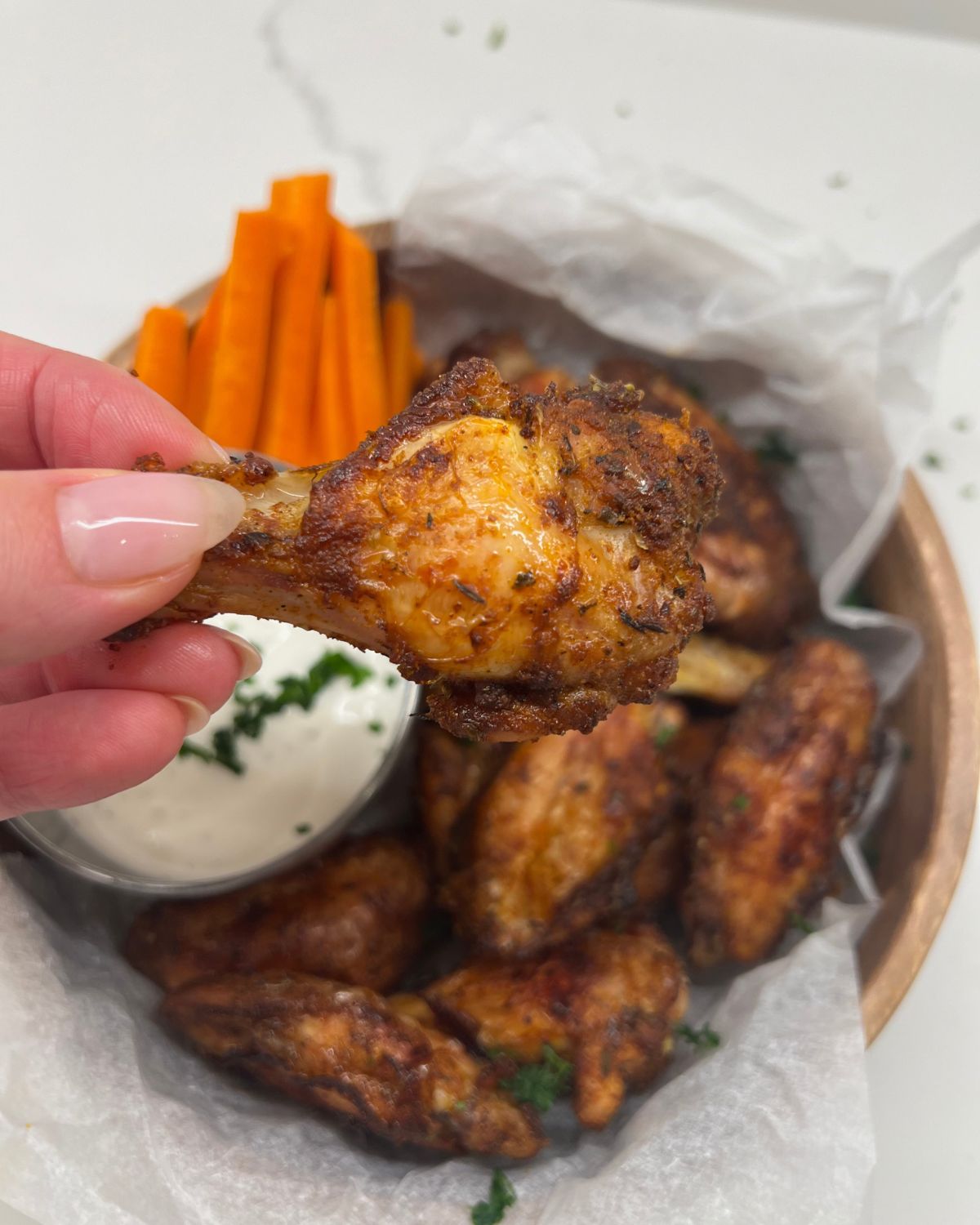 bowl of chicken wings and one being held up dipped in ranch 