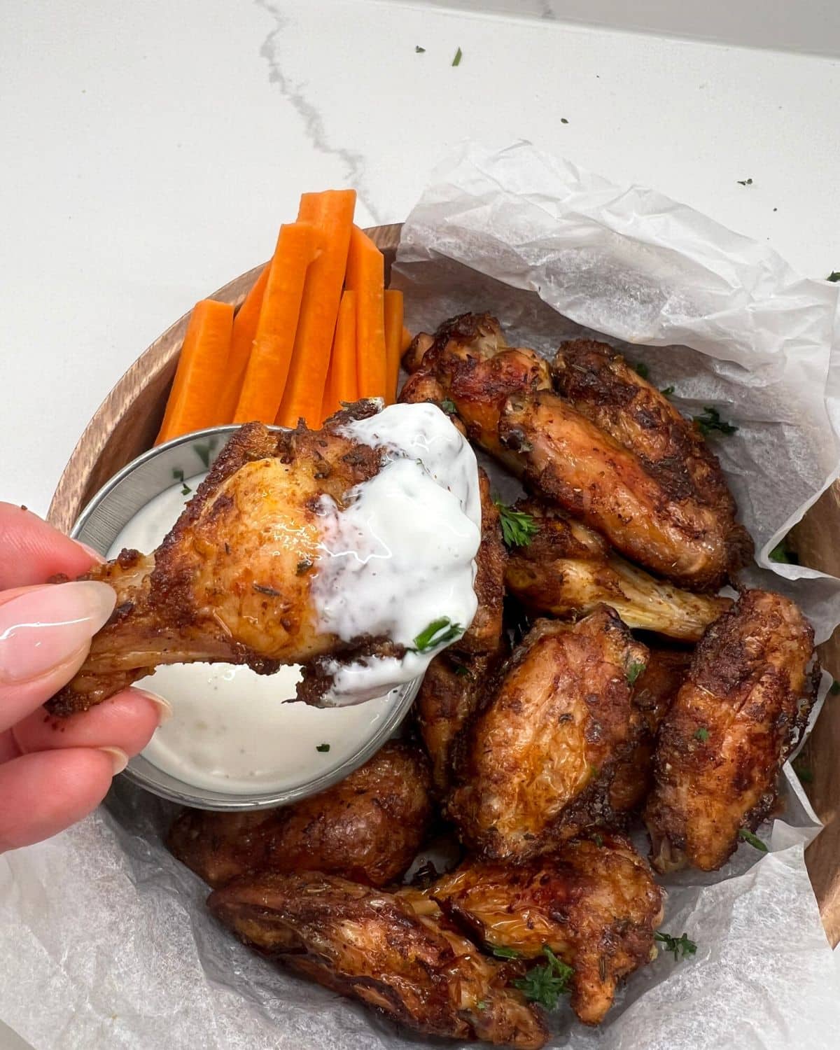 bowl of chicken wings and one being held up dipped in ranch 