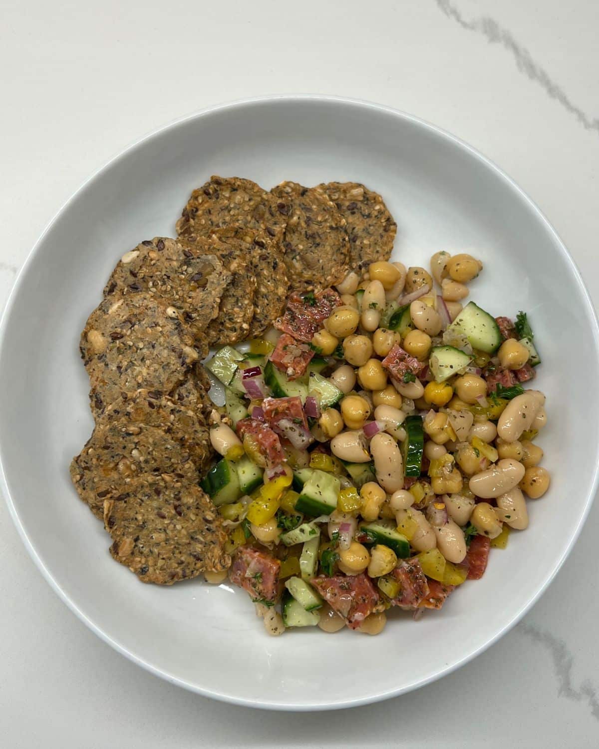 bean salad in white bowl with whole grain crackers 