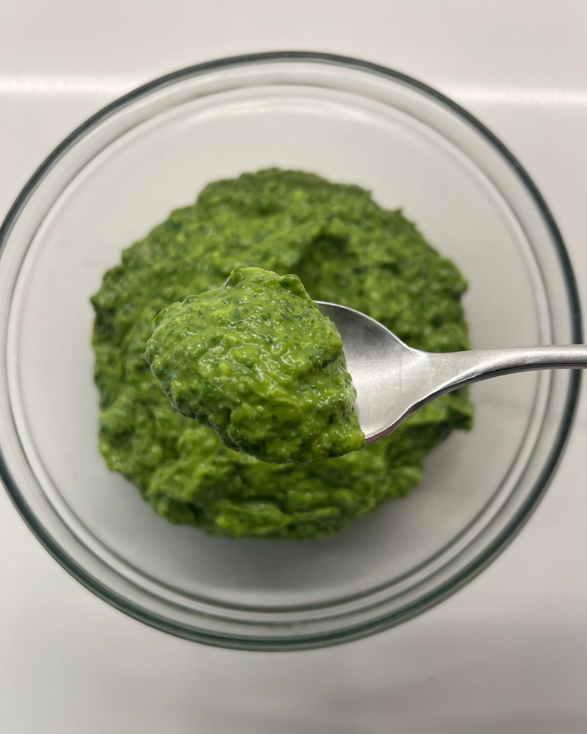 green sauce pesto in a bowl spoon scooping a bit out to show camera 