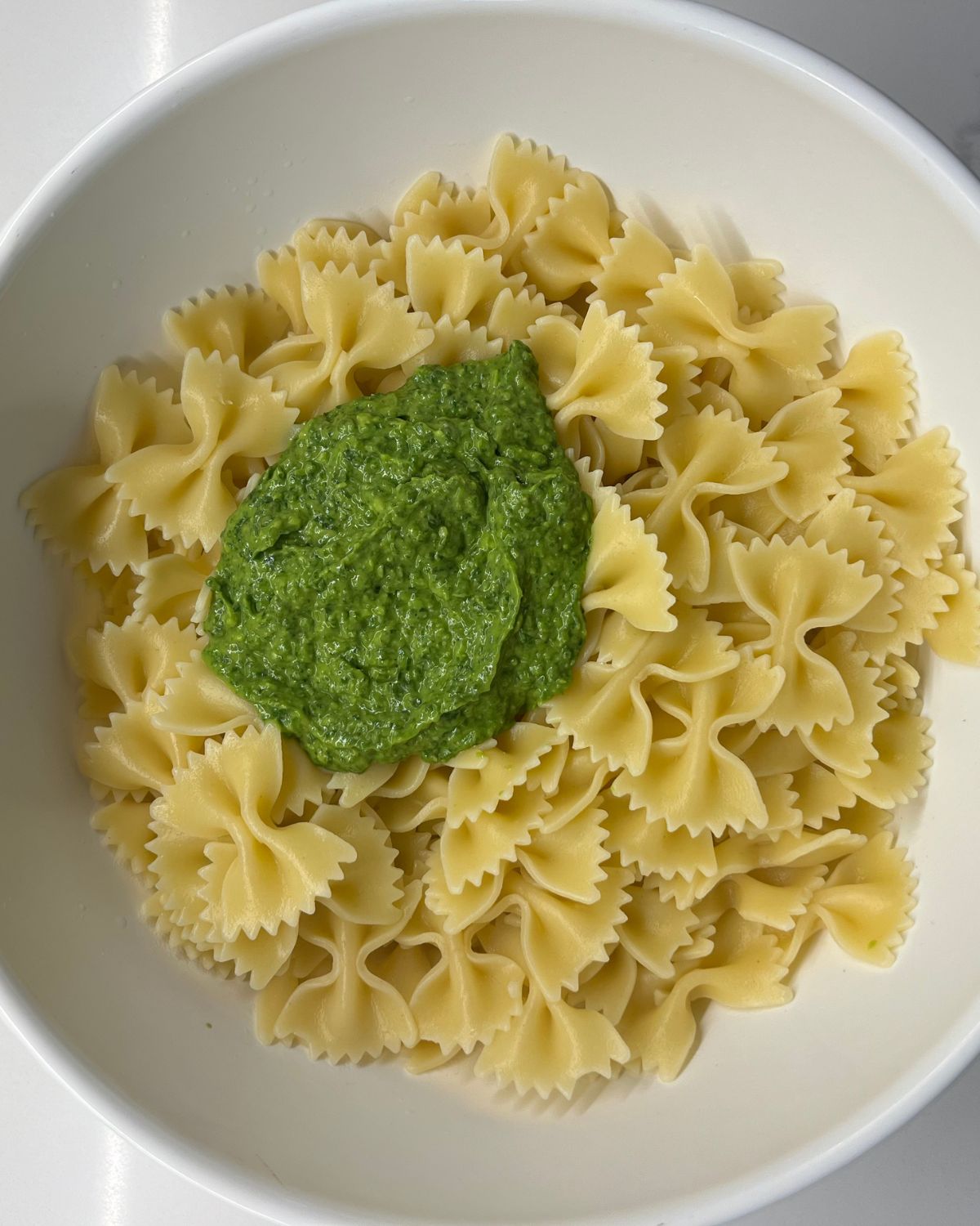 bow tie pasta in a bowl with the green sauce pasta scooped in but has not been mixed yet 