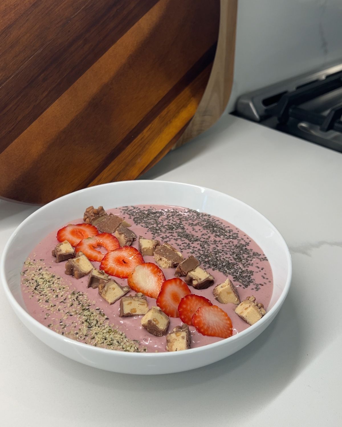 Smoothie bowl final product in a big white bowl topping with hemp, chia, granola bar and strawberries 