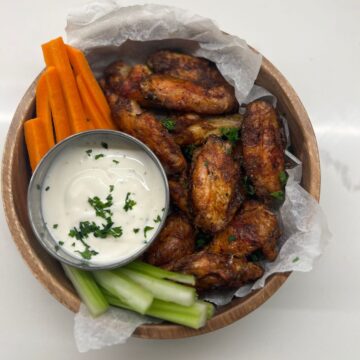 Chicken wings in bowl with ranch dip on side and carrot and celery sticks