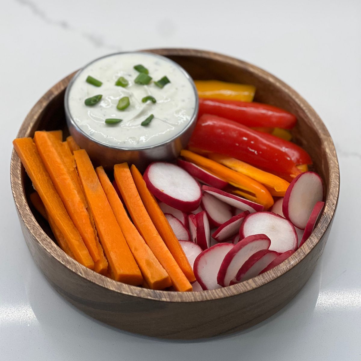 ranch dip in a bowl inside a bigger bowl with chopped carrots, peppers and radish