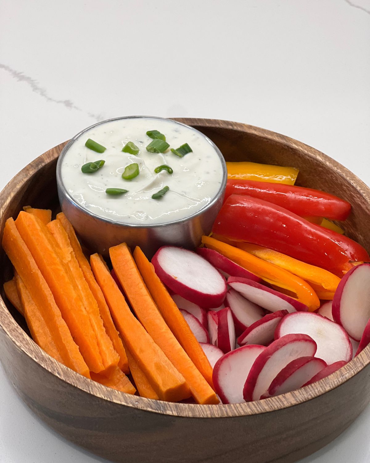 ranch dip in a bowl inside a bigger bowl with chopped carrots, peppers and radish