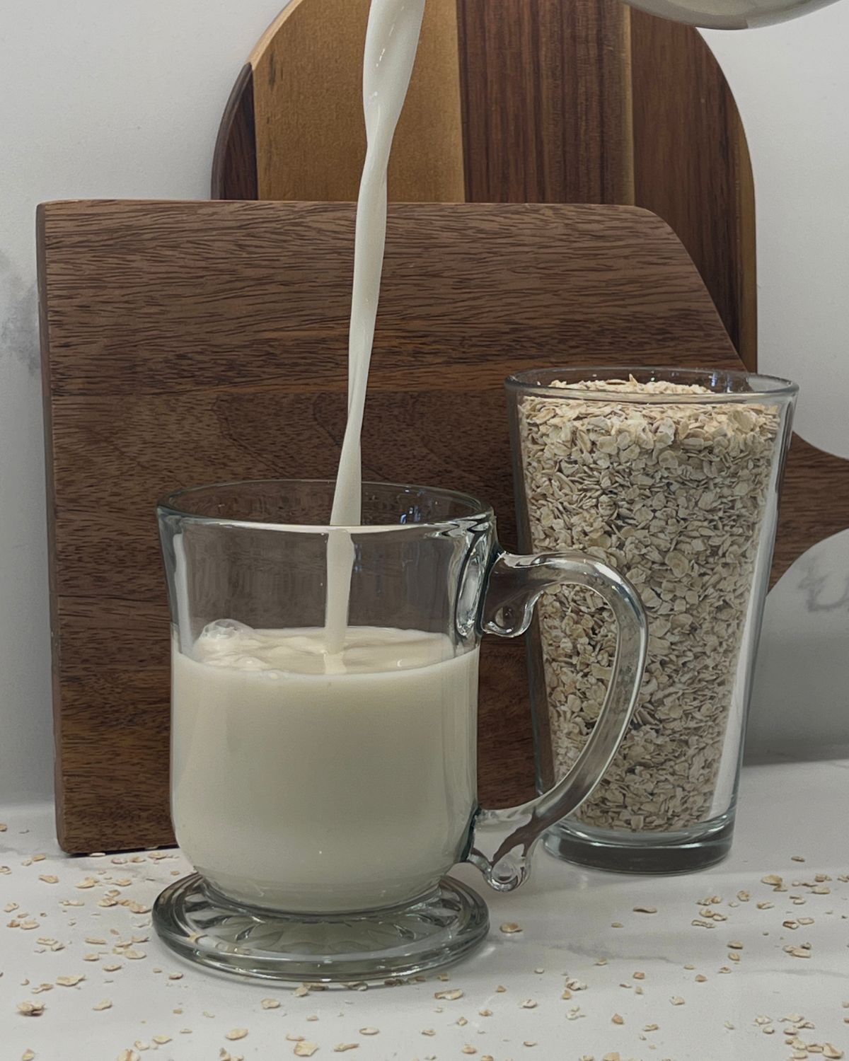 oat-milk being poured into big mug with cup of oats in the back  