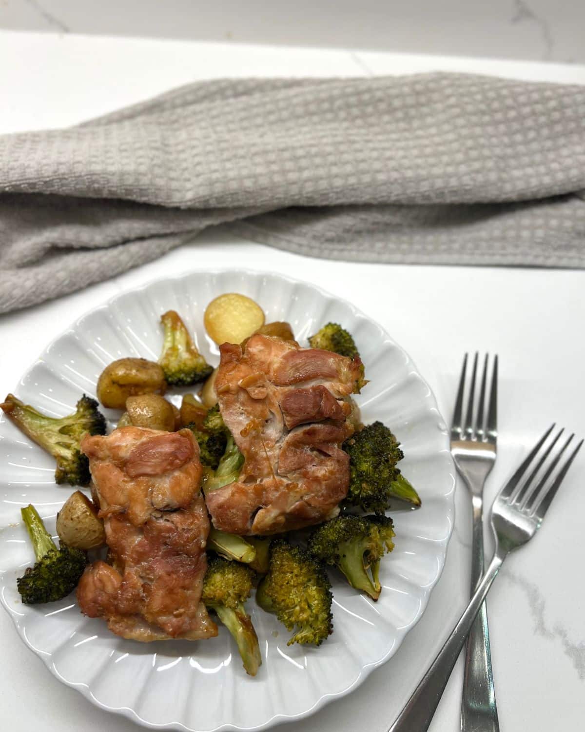 2 chicken thighs on a plate with potatoes and broccoli