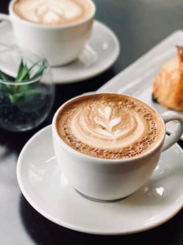 nice picture of a latte in nice white mug on white plate with pretty design on the latte