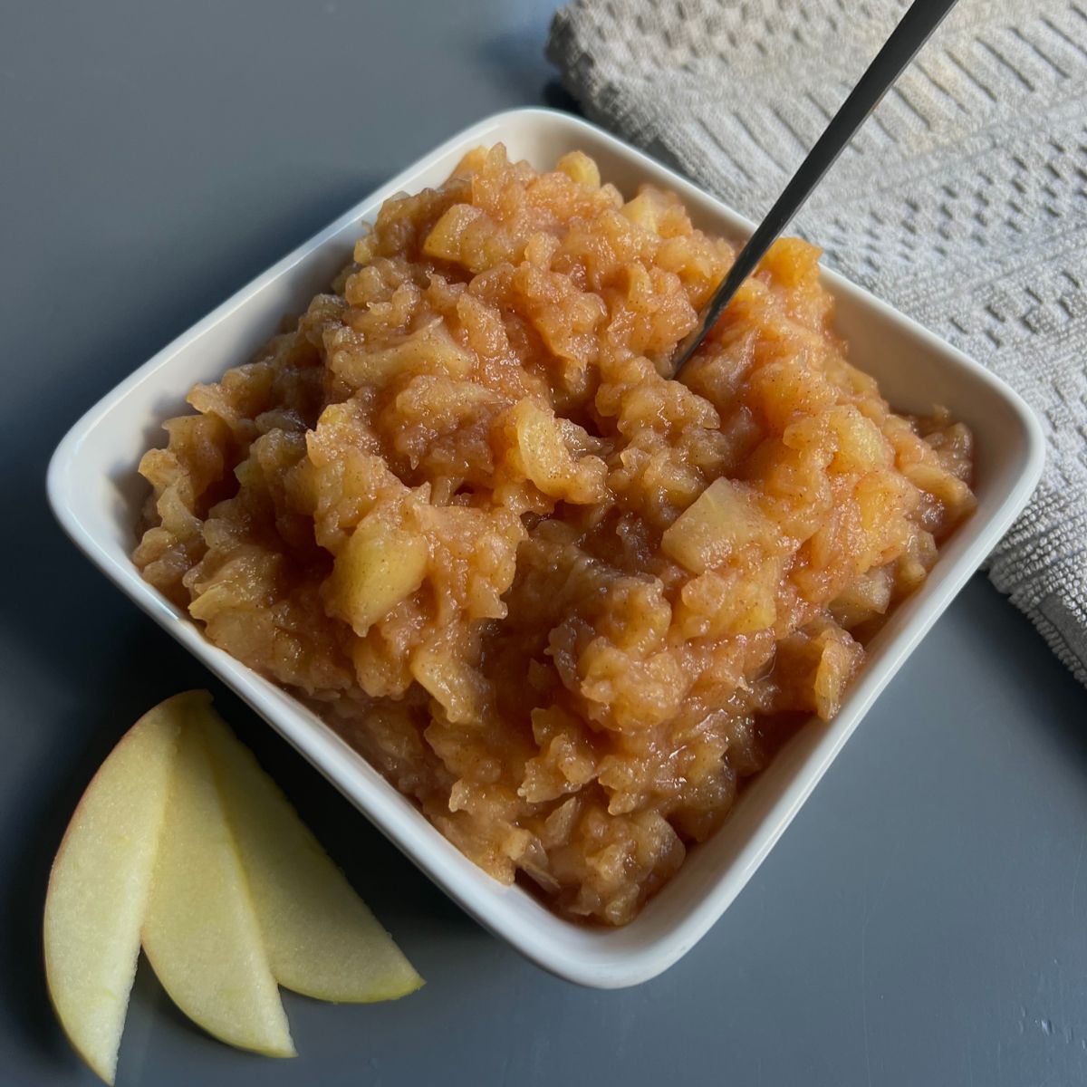 apple sauce in square bowl with some slices of apple on the side and spoon in