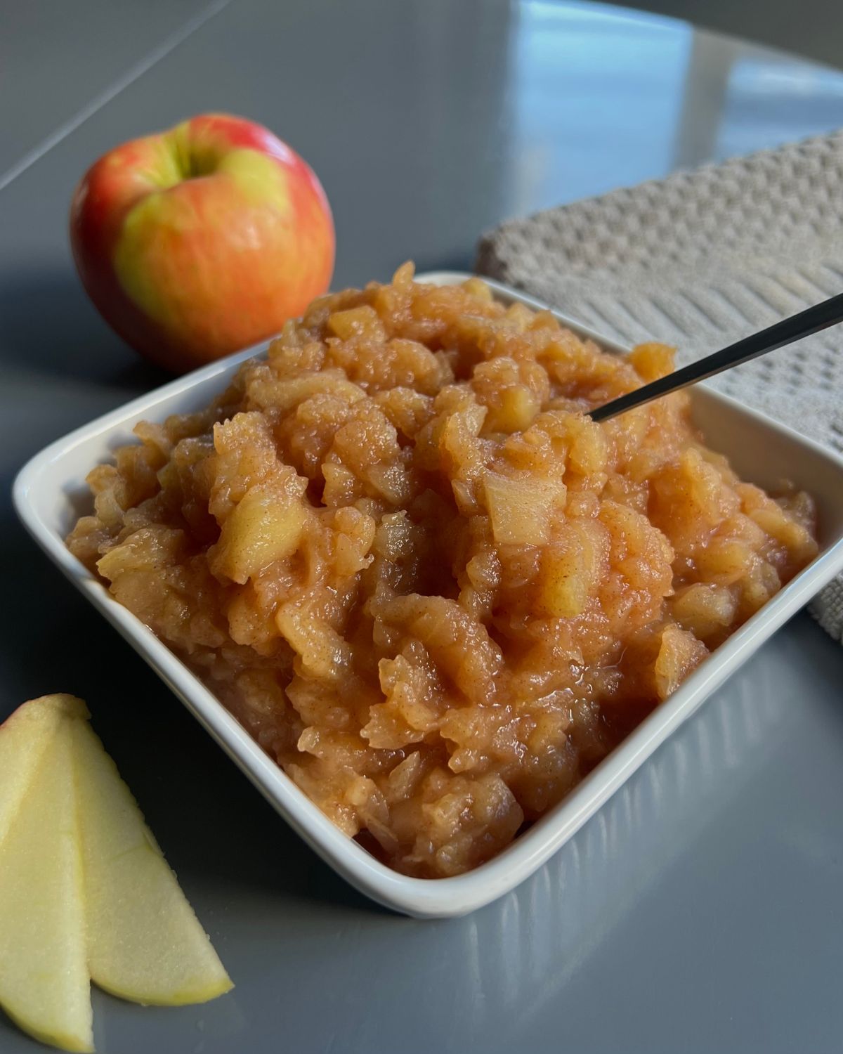 apple sauce in square bowl with slices of apple and an apple in the back