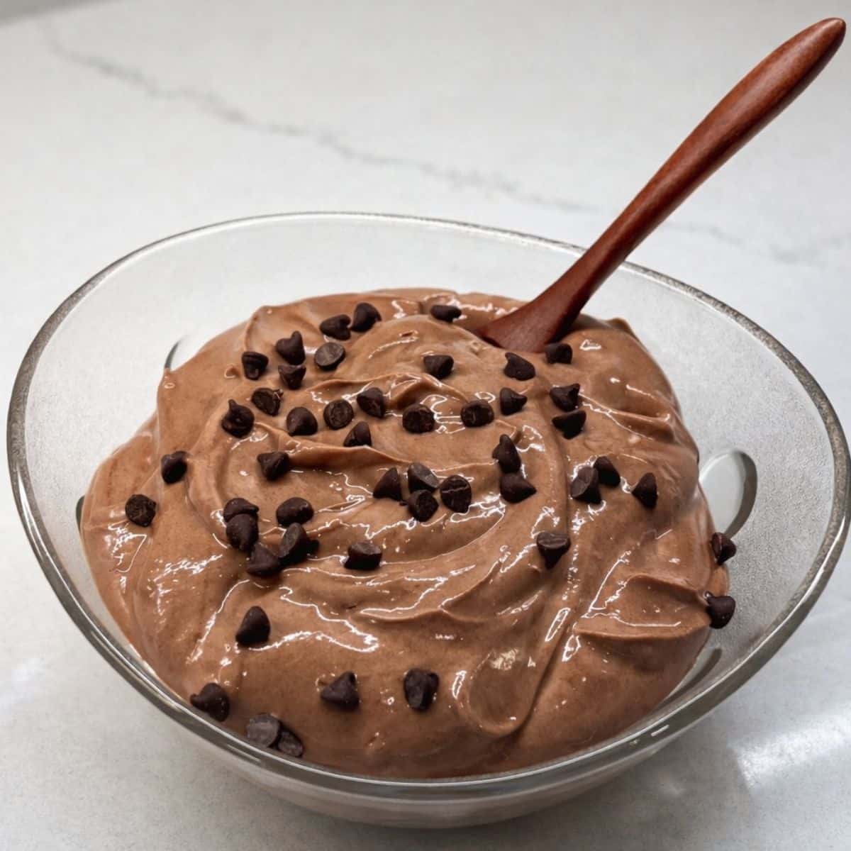 bowl of chocolate greek yogurt topped with mini chocolate chips with wooden spoon in