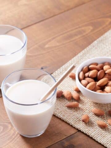 2 glasses of almond milk with a bowl of almonds on the side