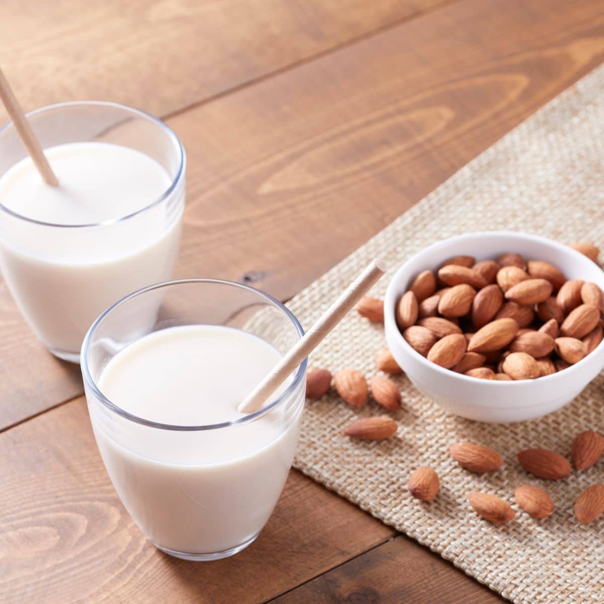 2 glasses of almond milk with a bowl of almonds on the side