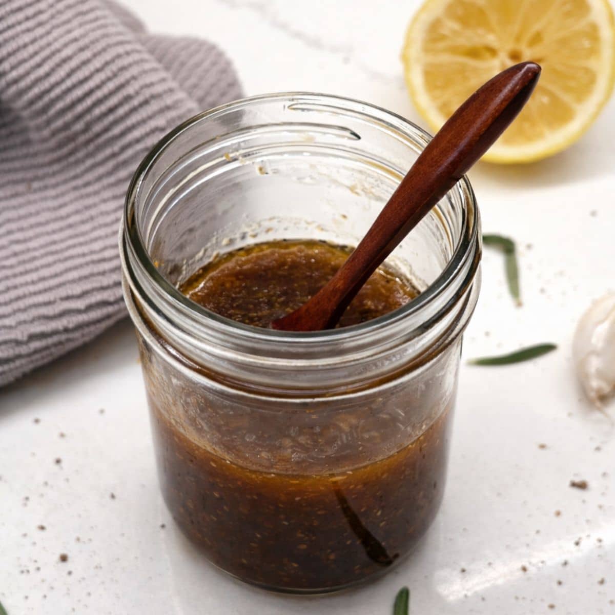 lemon dressing in mason jar with half lemon behind and grey cloth